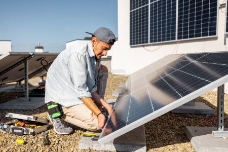 Foto de Hombre instalando paneles solares en el techo de su casa, atornillando la celda en la azotea plana para el autoconsumo. Concepto de energía renovable y sostenibilidad - Imagen libre de derechos