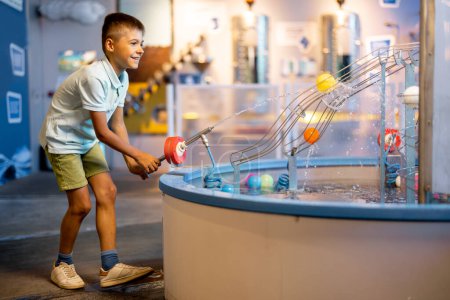 Niño juega con pelotas, aprendiendo fenómenos físicos de una manera interesante, divirtiéndose en un museo de ciencias con modelos interactivos