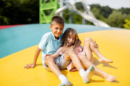 Foto de Retrato de un niño con su hermana pequeña abrazándose juntos, mientras pasaban el verano en el parque de atracciones - Imagen libre de derechos