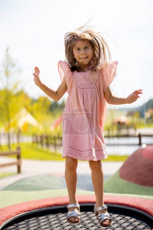 Téléchargez les photos : Petite fille sautant sur le trampoline gonflable, s'amusant visitant le parc d'attractions pendant des vacances d'été - en image libre de droit
