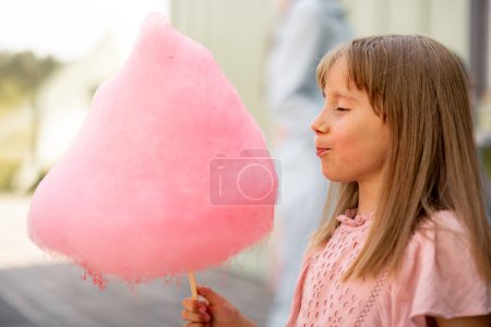 Foto de Niña feliz sostiene caramelo de algodón rosa mientras visita el parque de atracciones durante unas vacaciones de verano - Imagen libre de derechos