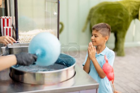 Foto de Niño esperando a que un dulce algodón de azúcar se haga en el mostrador mientras visita el parque de atracciones durante unas vacaciones de verano - Imagen libre de derechos