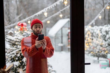 Photo for Man using phone while standing near Chrustmas tree at snowy backyard - Royalty Free Image