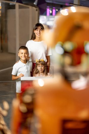 Foto de Mamá con los niños están emocionados de interactuar con un robot, visitando juntos el museo de ciencias. Concepto de tecnologías modernas y educación infantil - Imagen libre de derechos