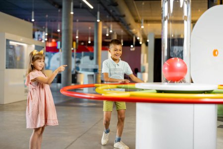 Foto de El niño y la niña aprenden física interactivamente en un modelo que muestra fenómenos físicos mientras visitan un museo de ciencias. Concepto de entretenimiento y aprendizaje infantil - Imagen libre de derechos
