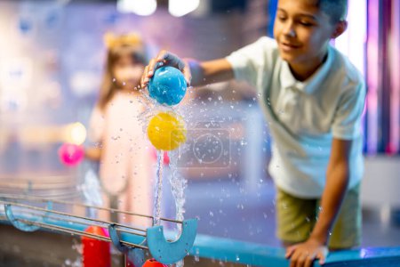 Kleiner Junge spielt mit Ball auf Wasserdampf, lernt auf interessante Weise physikalische Phänomene und hat Spaß in einem naturwissenschaftlichen Museum mit interaktiven Modellen