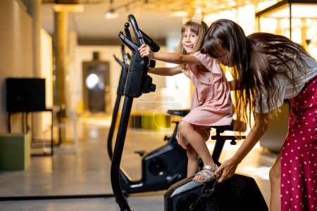 Photo for Little girl with mom training on bicycle simulator, visiting science museum. Concept of childrens education and entertainment - Royalty Free Image