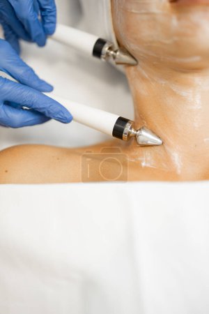 Foto de Mujer joven durante el procedimiento de microcorriente facial, vista de cerca en el cuello y electrodos especiales. Faciales de microcorriente para el efecto de elevación, tratamiento de la piel de belleza - Imagen libre de derechos
