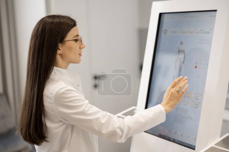 Téléchargez les photos : Portrait d'un médecin touchant l'écran de la machine à analyser le corps au salon de beauté. Concept de technologies modernes dans l'industrie de la médecine et la beauté - en image libre de droit