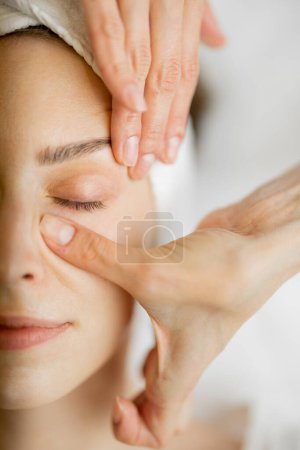 Téléchargez les photos : Femme adulte bénéficiant d'un massage facial relaxant, vue rapprochée sur le visage des femmes lors d'un massage. Massage de la zone sous les yeux - en image libre de droit