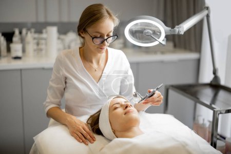 Téléchargez les photos : Jeune cosmétologue effectue la mésothérapie de l'oxygène sur le visage des femmes au salon de beauté. Concept de traitement non invasif et revitalisant de la peau - en image libre de droit