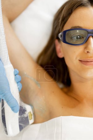 Foto de Mujer joven durante el procedimiento de depilación en sus axilas en el salón de belleza. Epilación láser y concepto de cuidado de la piel - Imagen libre de derechos