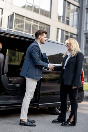 Photo for Female chauffeur greets the businessman while helping him to get out of the minivan taxi. Concept of personal driver, luxury taxi for business people - Royalty Free Image