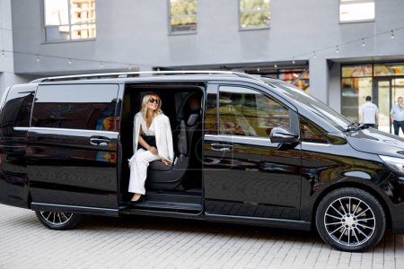 Foto de Elegante mujer de negocios en blanco mira desde un taxi minivan. Concepto de viajes de negocios y transporte - Imagen libre de derechos