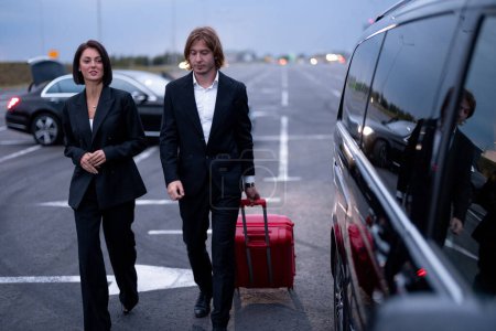 Téléchargez les photos : Couple d'affaires marchant avec une valise sur le parking, arrivé en taxi de luxe. Concept de transport et voyages d'affaires - en image libre de droit