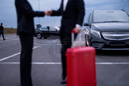 Foto de Pareja de negocios estrechándose la mano mientras están de pie con una maleta en el estacionamiento. Concepto de transporte y viajes de negocios - Imagen libre de derechos