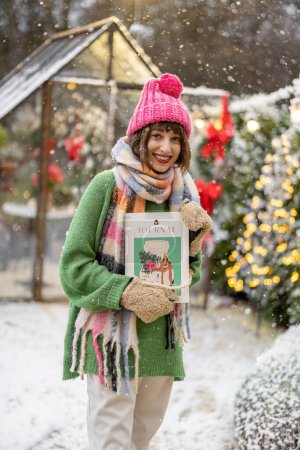 Photo for Portrait of a young woman holding magazine with New Years cover at snowy backyard decorated for a winter holidays - Royalty Free Image