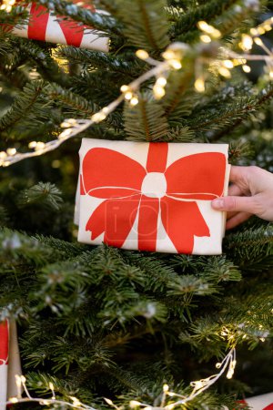 Téléchargez les photos : Femme décore l'arbre de Noël avec de grands arcs rouges et guirlande, gros plan. Concept de décorations et ambiance festive - en image libre de droit