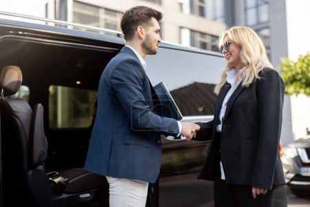 Photo for Female chauffeur greets the businessman while helping him to get out of the minivan taxi. Concept of personal driver, luxury taxi for business people - Royalty Free Image