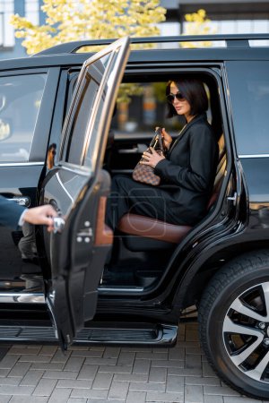Foto de Retrato de una elegante mujer de negocios en negro bajándose de un lujoso taxi SUV. Concepto de viajes de negocios y transporte - Imagen libre de derechos