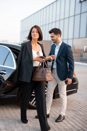 Photo for Businessman helps gently a woman to get out of a car, arrived by luxury vehicle for some event at evening. Concept of transportation and business lifestyle - Royalty Free Image