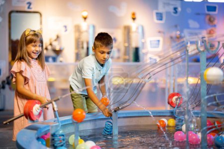 Niño y niña juegan con pelotas, aprendiendo fenómenos físicos de una manera interesante, divirtiéndose en un museo de ciencias con modelos interactivos
