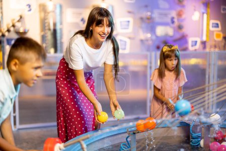 Téléchargez les photos : Maman avec les enfants jouent avec les balles, apprendre les phénomènes physiques d'une manière intéressante, s'amuser dans un musée des sciences avec des modèles interactifs - en image libre de droit