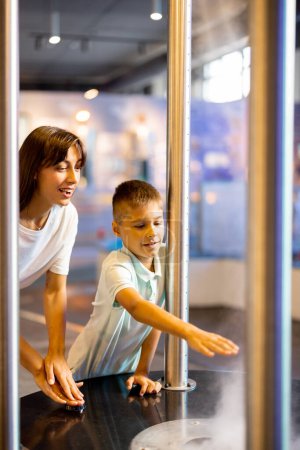 Photo for Mom with a little boy learn physics interactively on a model that shows physical phenomena while visiting a science museum. Concept of childrens entertainment and learning - Royalty Free Image