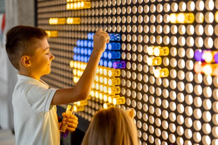 Foto de Niños haciendo una foto con fichas de colores en la pared, jugando en modelos interactivos en el museo de ciencias. Concepto de entretenimiento y aprendizaje infantil - Imagen libre de derechos