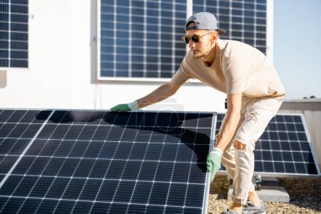 Foto de Hombre instalando paneles solares en el techo de su casa, ajustando la celda en la azotea plana para el autoconsumo. Concepto de energía renovable y sostenibilidad - Imagen libre de derechos