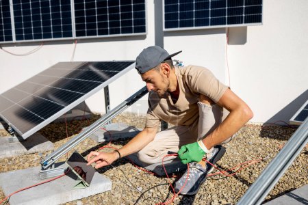 Téléchargez les photos : Un électricien ou un technicien vérifie la fonctionnalité d'une station solaire sur le toit d'une maison privée. Homme installant des panneaux solaires sur un toit de sa maison - en image libre de droit