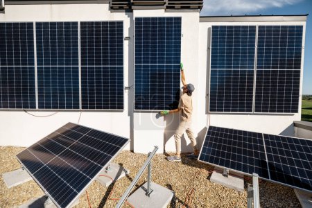 Foto de Hombre instalando paneles solares en la pared vertical en una azotea de su casa para el autoconsumo. Concepto de energía renovable y sostenibilidad - Imagen libre de derechos