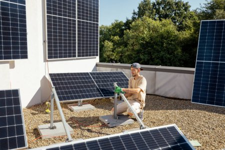 Téléchargez les photos : L'homme installe des supports pour panneaux solaires sur un toit de la maison. Propriétaire de la propriété installant des panneaux solaires pour l'autoconsommation - en image libre de droit