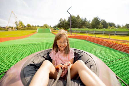 Foto de Niña feliz desciende en tubo de trineo inflable en una pista de verano, divirtiéndose en el parque de atracciones. Concepto de vacaciones de verano y entretenimiento infantil - Imagen libre de derechos