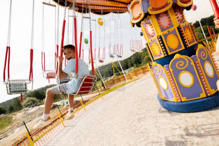 Photo for Boy riding on colorful amusement carousel while visiting amusement park during a summer vacation - Royalty Free Image