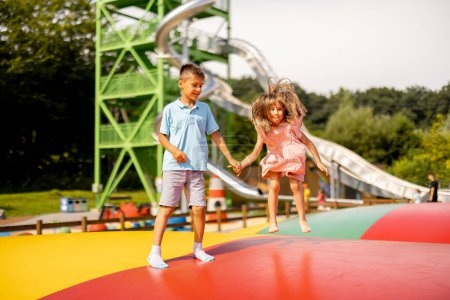 Photo for Kids jumping on inflatable trampoline, having fun visiting amusement park during a summer vacation. Brother with a sister spending leisure time together - Royalty Free Image