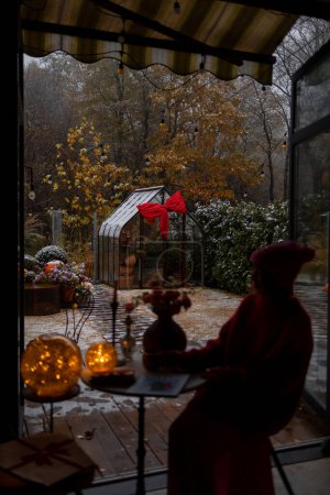 Téléchargez les photos : Femme s'assoit à la table et profite des vacances d'hiver dans la cour arrière de sa maison. Vacances d'hiver et concept d'humeur - en image libre de droit