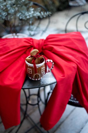 Photo for Festive cup with gingerbread cookie on table with red bow outdoors. Homemade gingerbreads and festive cup on table at home. Winter holidays mood and decorations concept - Royalty Free Image