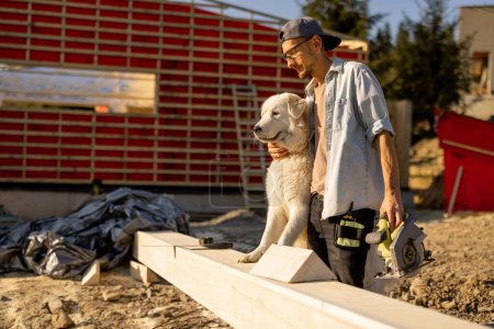 Téléchargez les photos : Homme avec son chien sur le chantier, s'amuser ensemble tout en construisant une maison en bois - en image libre de droit