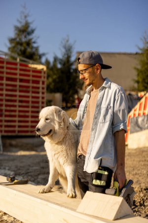 Téléchargez les photos : Homme avec son chien sur le chantier, s'amuser ensemble tout en construisant une maison en bois - en image libre de droit