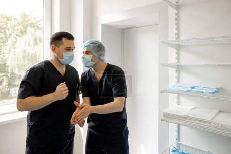 Foto de Dos cirujanos con máscaras faciales hablan y se divierten mientras se preparan para la operación quirúrgica. Concepto de esterilidad y cirugía - Imagen libre de derechos