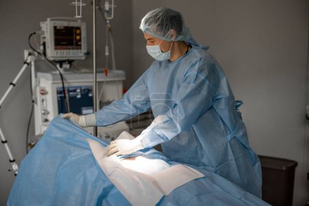 Foto de El cirujano se prepara para la operación, cubriendo al paciente con un desgaste estéril. Concepto de esterilidad durante el tratamiento quirúrgico y el procedimiento invasivo - Imagen libre de derechos