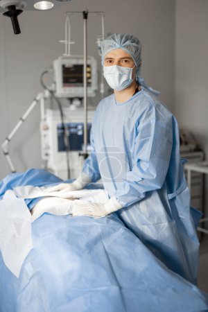 Photo for Portrait of a surgeon in sterile uniform ready for an operation standing near a patient lying in operating room. Concept of sterility during surgical treatment and invasive procedure - Royalty Free Image
