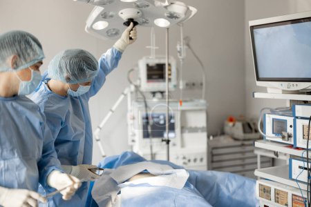 Foto de Los cirujanos instalan una luz, preparándose para un procedimiento invasivo en la sala de operaciones. Concepto de tratamiento quirúrgico - Imagen libre de derechos