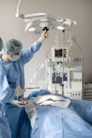 Téléchargez les photos : Les chirurgiens installent une lumière, se préparant à une intervention invasive en salle d'opération. Concept de traitement chirurgical - en image libre de droit