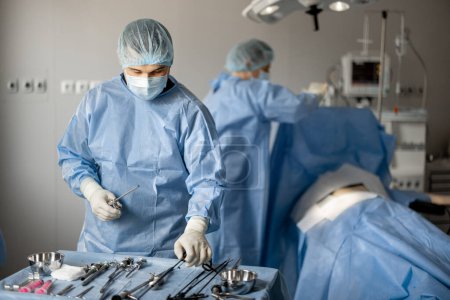 Photo for Surgeons in uniform prepare sterile medical instruments for surgery, ready to operate a patient in the operating room. Concept of invasive treatment - Royalty Free Image