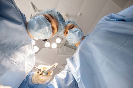 Foto de Cirujanos confiados mirando a la cámara mientras operan a un paciente. Idea de cirugía y tratamientos invasivos - Imagen libre de derechos