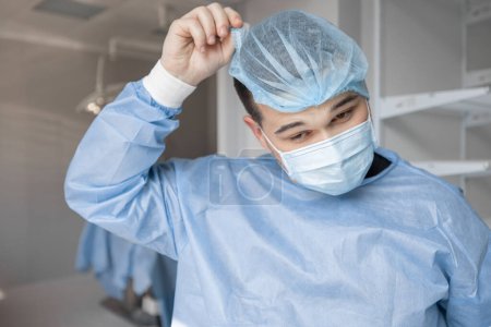 Photo for Portrait of a tired surgeon taking off his hat after hard surgery, while leaving an operating room - Royalty Free Image