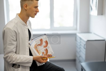 Foto de Retrato de un joven médico como gastroenterólogo con un libro en el consultorio médico - Imagen libre de derechos