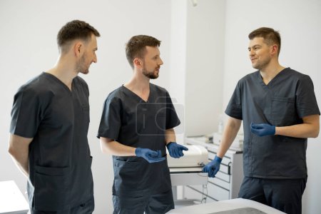 Photo for Council of three young and cheerful surgeons in a medical office. Concept of teamwork and professional medical treatment - Royalty Free Image